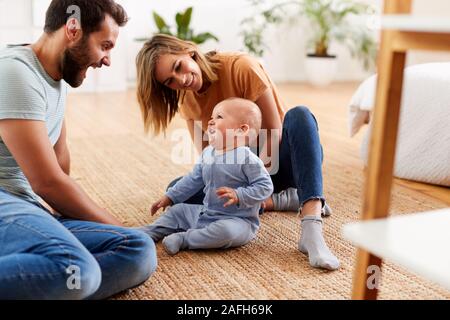 Les parents assis sur le plancher à la maison à jouer avec son bébé Banque D'Images