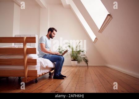 Jeune homme assis sur le lit dans un appartement Loft Working On Laptop Banque D'Images