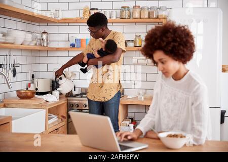 Multitâche Père Fils Bébé détient et verse un verre comme mère utilise le coffre et mange le petit déjeuner Banque D'Images