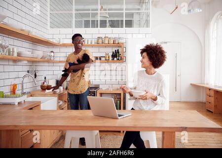 Multitâche Père Fils Bébé détient et nettoie la surface comme mère utilise le coffre et mange le petit déjeuner Banque D'Images