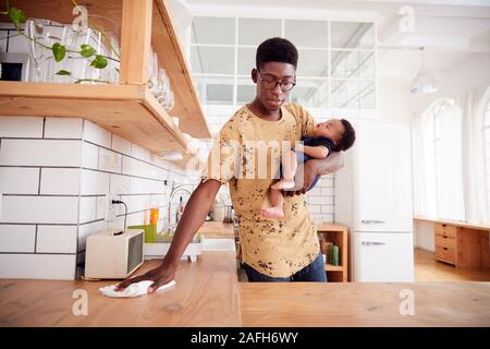 Multitâche père détient bébé endormi Fils et nettoie dans la cuisine Banque D'Images