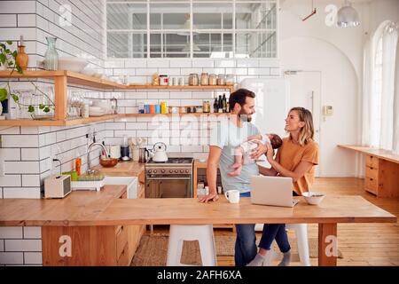 Famille occupée dans la cuisine au petit-déjeuner avec le père s'occuper de son bébé Banque D'Images