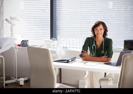 Portrait Of Smiling Female Doctor with Stethoscope Sitting Behind Desk In Office Banque D'Images