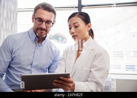 Femme Médecin montrant les résultats des tests des patients de sexe masculin sur Digital Tablet In Office Banque D'Images
