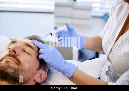 Coiffeur femme mature donnant Male Patient injection de Botox Dans le Front Banque D'Images