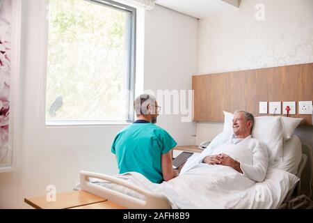 Surgeon With Digital Tablet Visiter Senior Male Patient In Hospital Bed en unité de Gériatrie Banque D'Images