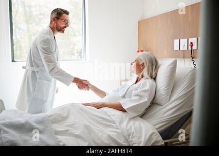 Visiter chirurgien et serrer la main de femme mature Patient In Hospital Bed Banque D'Images