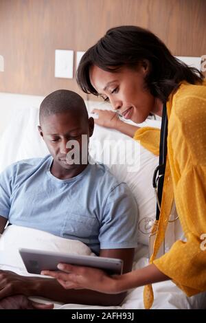 Médecin avec tablette numérique visiter et parler avec Male Patient In Hospital Bed Banque D'Images