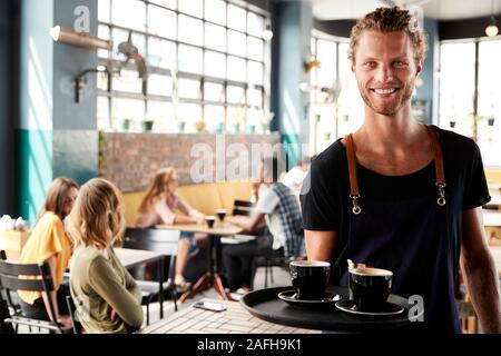 Portrait Of Waiter Serving Customers In Busy Coffee Shop Banque D'Images
