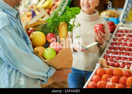 Close up of modern couple de choisir des légumes frais tout en appréciant de shopping dans le marché, l'accent sur sac de papier avec des provisions en premier plan, Banque D'Images