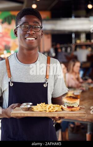 Portrait Of Waiter Serving Food à des clients dans le bar-restaurant animé Banque D'Images