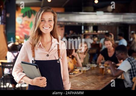 Portrait Of Waitress Holding spéciaux servant Busy Bar Restaurant Banque D'Images