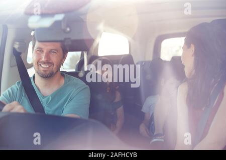 Famille de quatre jeunes blancs dans leur voiture, maman tournant pour parler aux enfants, vu à travers pare-brise avant Banque D'Images