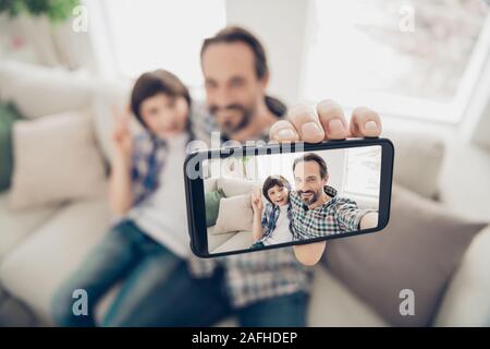 Phto portrait of handsome gaie positive père hugging embrassant son fils sur la table en tenant le téléphone selfies montrant v-sign avoir meilleur week-end Banque D'Images
