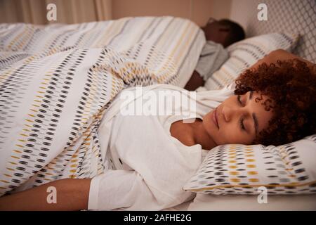 Millennial African American Woman lying on her back endormi dans son lit, sa partenaire dans l'arrière-plan Banque D'Images