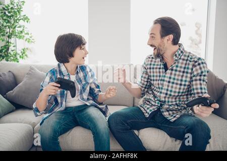 Portrait de deux beaux gars Gai gai satisfait attrayant père et fils pré-ado assis sur le canapé à jouer en ligne jeu gagnant à la lumière moderne blanc Banque D'Images