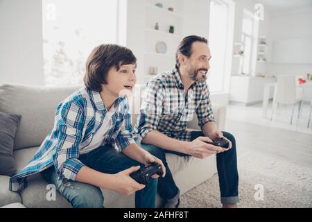 Portrait de profil Vue de côté deux beaux gars Gai gai attrayant père et fils pré-ado assis sur le canapé à jouer jeu en ligne prévues le week-end au Banque D'Images