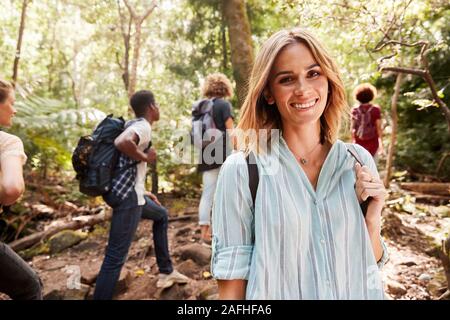 Waist up portrait of smiling woman blanc millénaire de la randonnée dans une forêt avec ses amis, Close up Banque D'Images