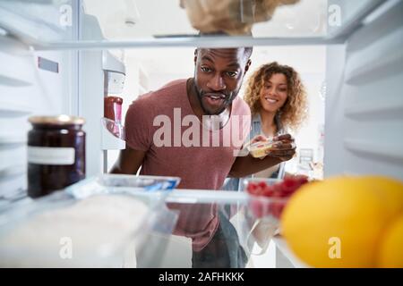 À la vue de l'intérieur du réfrigérateur en Couple Ouvrez la porte et déballez votre sac de nourriture Banque D'Images