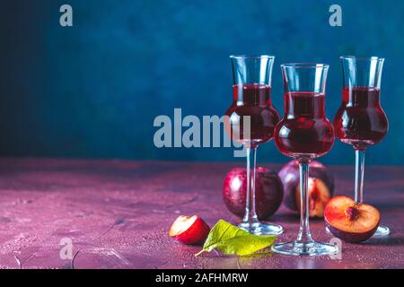 Les prunes strong boisson alcoolisée dans grappas wineglass de rosée. Alcools, slivovica, de prunes ou de prunes prunes mûres avec de la vodka sur le bleu foncé et bordeaux Banque D'Images