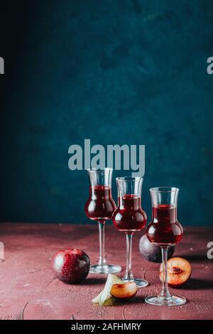 Les prunes strong boisson alcoolisée dans grappas wineglass de rosée. Alcools, slivovica, de prunes ou de prunes prunes mûres avec de la vodka sur le bleu foncé et bordeaux Banque D'Images