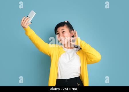 Asian teenager's portrait isolé sur fond studio bleu. Belle brunette model femme aux cheveux longs. Concept d'émotions humaines, expression du visage, ventes, ad. Décisions ou selfies vlog. Banque D'Images