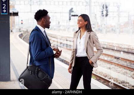 Businessman And Businesswoman pour se rendre à son travail en conversation sur un quai de gare en attente de Train Banque D'Images