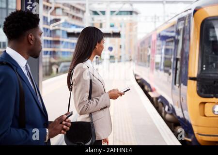 Businessman And Businesswoman pour se rendre à son travail sur un quai de gare en attente de Train Banque D'Images