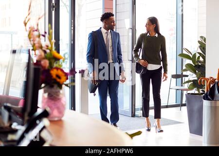 Businessman And Businesswoman arrivant pour travailler au bureau Walking Through Door Banque D'Images