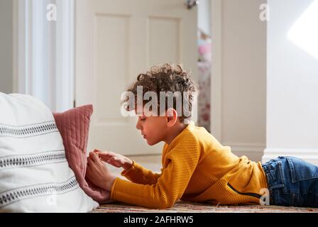 Garçon couché sur le plancher de chambre à passer trop de temps à l'aide de Mobile Phone Banque D'Images