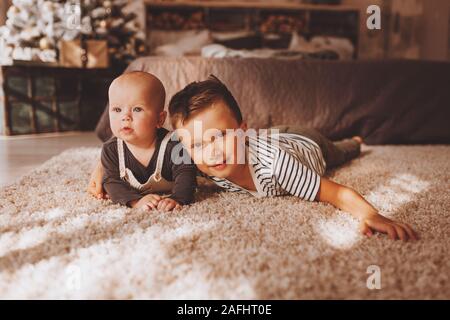 Heureux petit enfant avec son frère près de l'arbre de Noël et des lumières. Banque D'Images