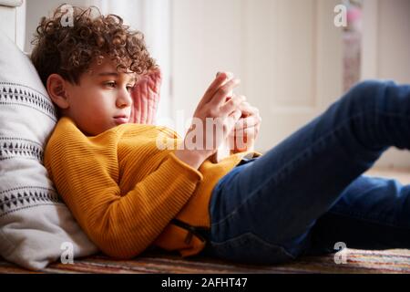 Garçon couché sur le plancher de chambre à passer trop de temps à l'aide de Mobile Phone Banque D'Images