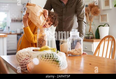 Père Fils aidant à remplir les contenants d'aliments à domicile à l'aide de l'emballage des déchets Zéro Banque D'Images
