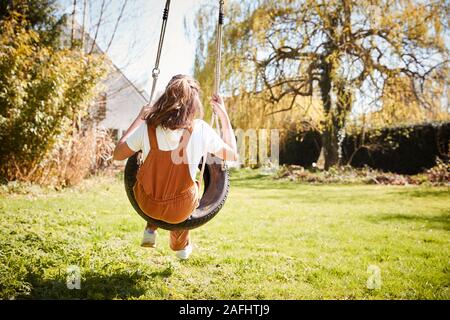 Vue arrière de l'amusement de fille sur balançoire pneu en jardin à la maison Banque D'Images