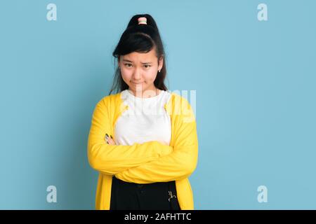 Asian teenager's portrait isolé sur fond studio bleu. Belle brunette model femme aux cheveux longs. Concept d'émotions humaines, expression du visage, ventes, ad. Posant avec les mains croisées. Banque D'Images