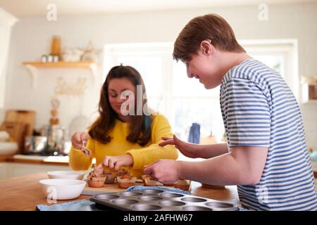 Les jeunes Trisomie Couple Decorating Cupcakes fait maison avec du glaçage dans la cuisine à la maison Banque D'Images