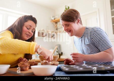 Les jeunes Trisomie Couple Decorating Cupcakes fait maison avec du glaçage dans la cuisine à la maison Banque D'Images