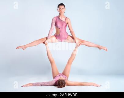 Deux gymnastes filles flexibles avec des nattes, en rose justaucorps sont l'exécution par le biais d'appuyer tout en se posant isolé sur fond blanc. Close-up. Banque D'Images