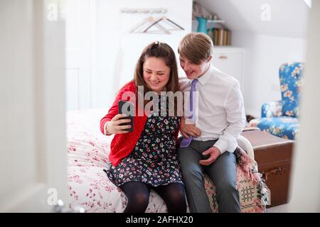 Aimer les jeunes Trisomie Couple Sitting on Bed Using Mobile Phone à prendre à la maison Selfies Banque D'Images