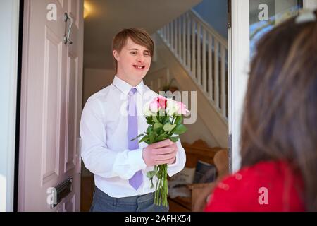 Jeune couple aimant le syndrome de Down à l'avant porte avec Man Giving Woman Flowers Banque D'Images