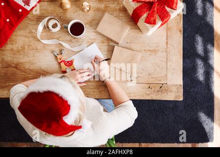 Passage tourné à la femme dans l'écriture sur carte de Noël et cadeau Emballage Wearing Santa Hat Banque D'Images