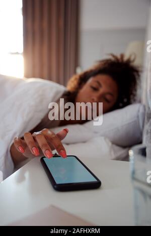 Woman Waking Up In Bed tend la main pour arrêter l'alarme sur téléphone mobile Banque D'Images