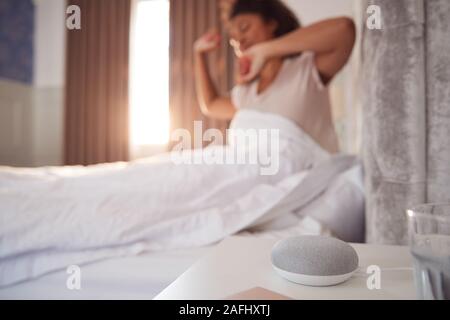 Woman Waking Up In Bed avec assistant vocal sur Table de chevet à côté d'elle Banque D'Images