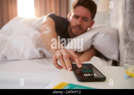 Man Waking Up In Bed tend la main pour arrêter l'alarme sur téléphone mobile Banque D'Images