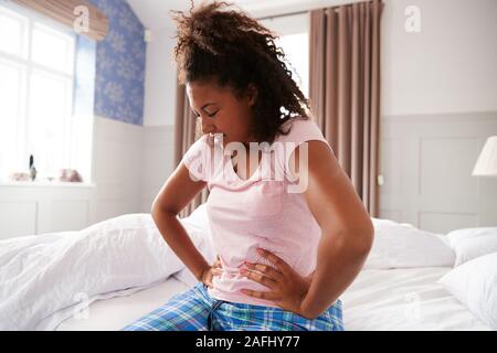 Woman Wearing Pajamas souffrant avec douleur Période assis sur le lit à la maison Banque D'Images