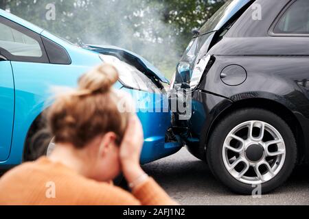 Automobiliste femelle avec la tête dans les mains assis à côté de véhicules impliqués dans un accident de voiture Banque D'Images