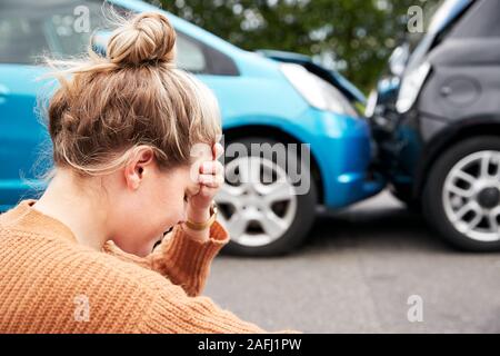 Automobiliste femelle avec la tête dans les mains assis à côté de véhicules impliqués dans un accident de voiture Banque D'Images