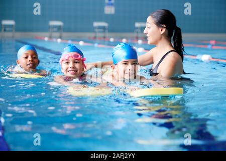 Entraîneuse en donnant de l'eau Groupe d'enfants leçon de natation en piscine couverte