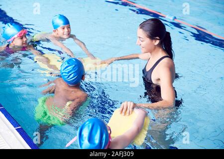 Entraîneuse en donnant de l'eau Groupe d'enfants leçon de natation en piscine couverte