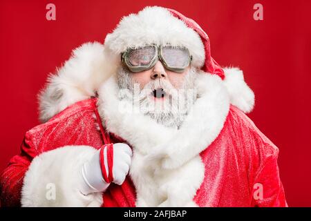 La photo en gros plan de l'impressionné personnes âgées fun santa sack sac de livrer les cadeaux stare voir catastrophe naturelle portent des gants blancs lunettes cap sur rouge isolé Banque D'Images